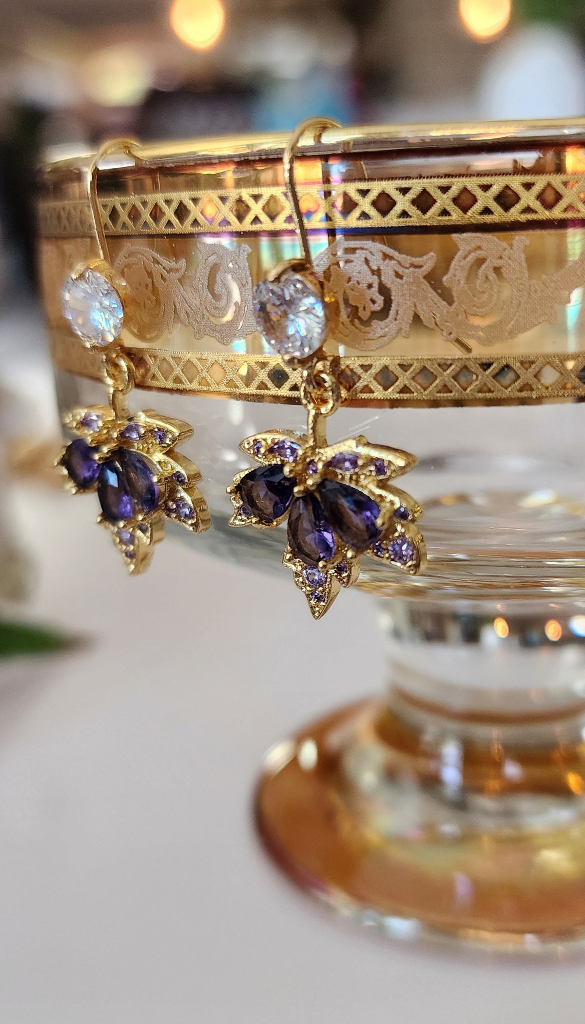 Gold maple leaf earrings with purple crystals on a decorative stand