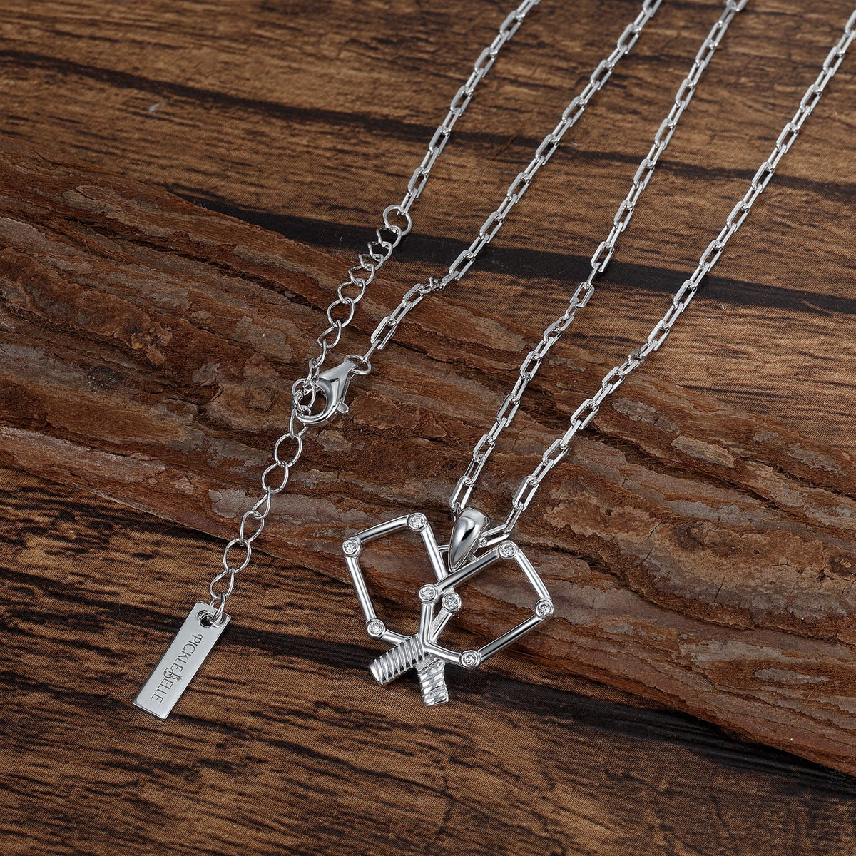 Silver necklace with pickleball paddle pendant on a wooden surface