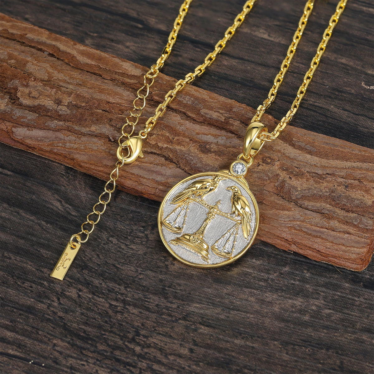 Gold and silver necklace with a zodiac Libra pendant depicting the classic Scale with two Ravens on a wooden surface