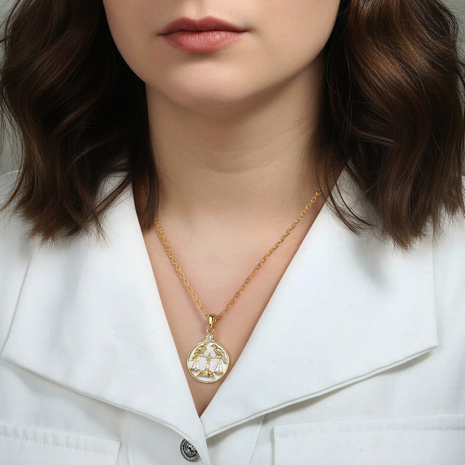 Woman wearing a gold and silver necklace with a Libra Zodiac pendant against a neutral background