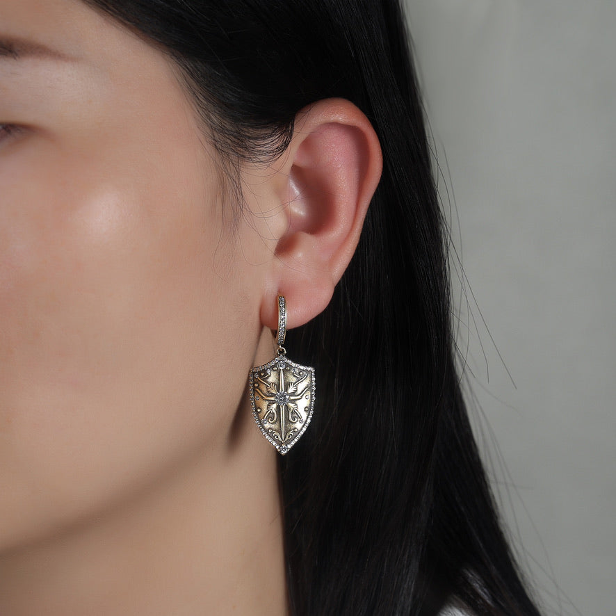 Close-up of a person wearing a decorative antique gold earring with a decorative shield design.
