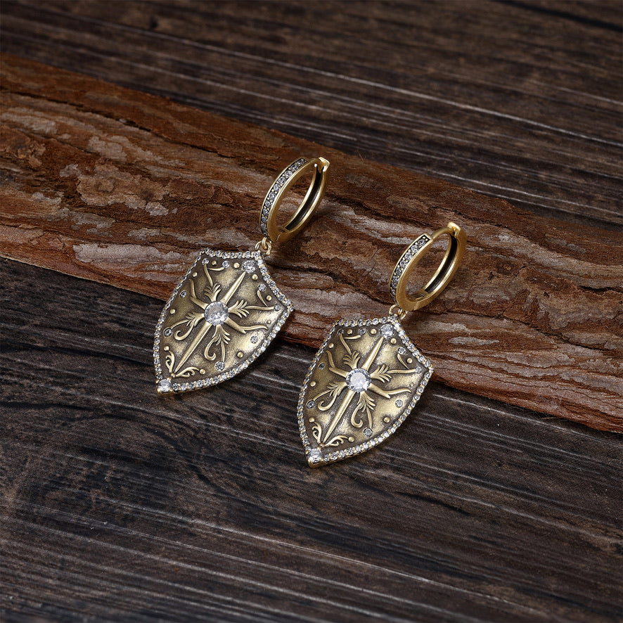 Antique Gold shield-shaped earrings with intricate designs on a wooden surface