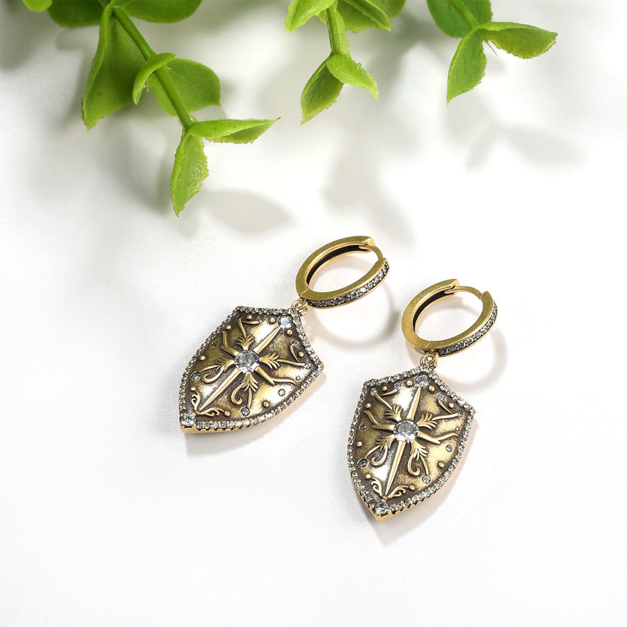 Antique Gold shield shaped earrings with intricate designs on a white surface