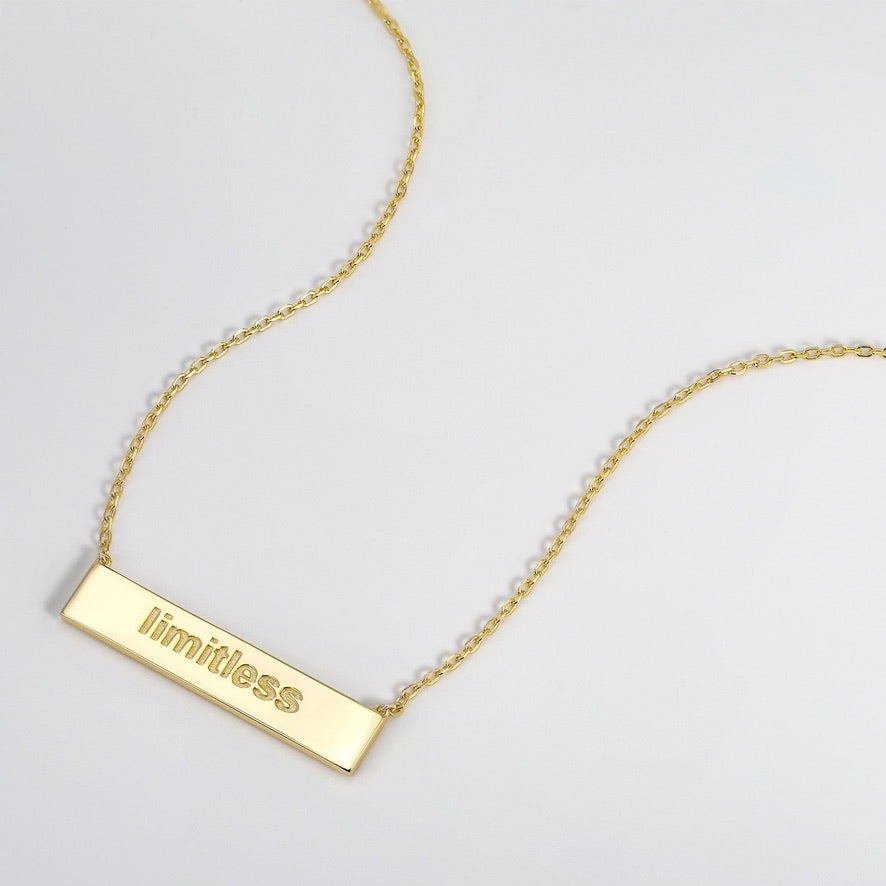 Gold necklace with a bar pendant displaying the word 'limitless' on a light gray background