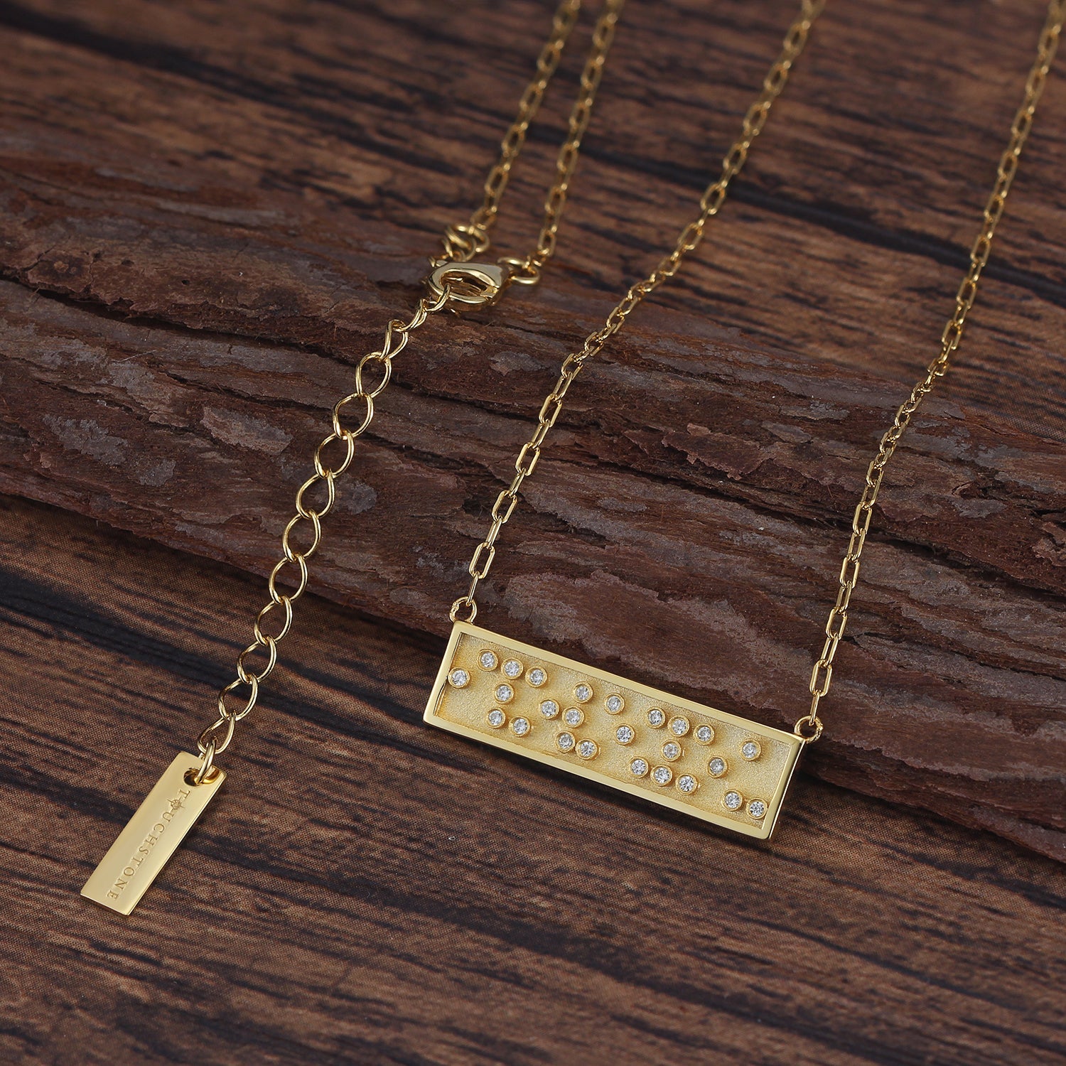 Touchstone I Love You Mini-Bar Necklace in Gold with Braille 'I Love You' in Crystals on wood surface