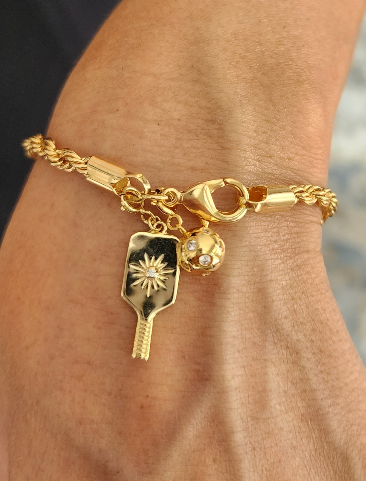 Gold bracelet with pickleball paddle and ball charm on wrist