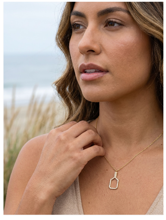 Woman wearing a gold pickleball paddle necklace with diamonds outdoors