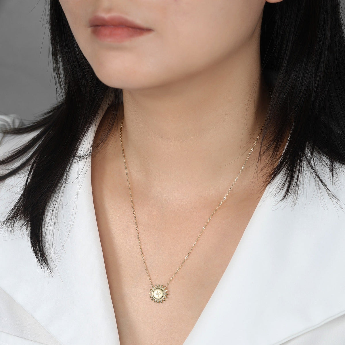 Close-up of a person wearing a delicate gold necklace with a sunburst friendship symbol pendant.