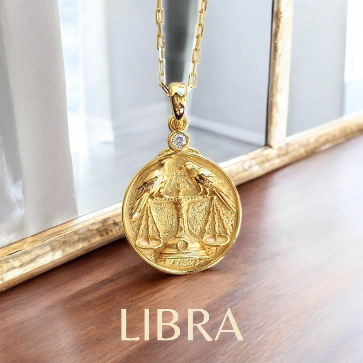 Gold Libra zodiac pendant showing two ravens on a scale necklace on a wooden surface