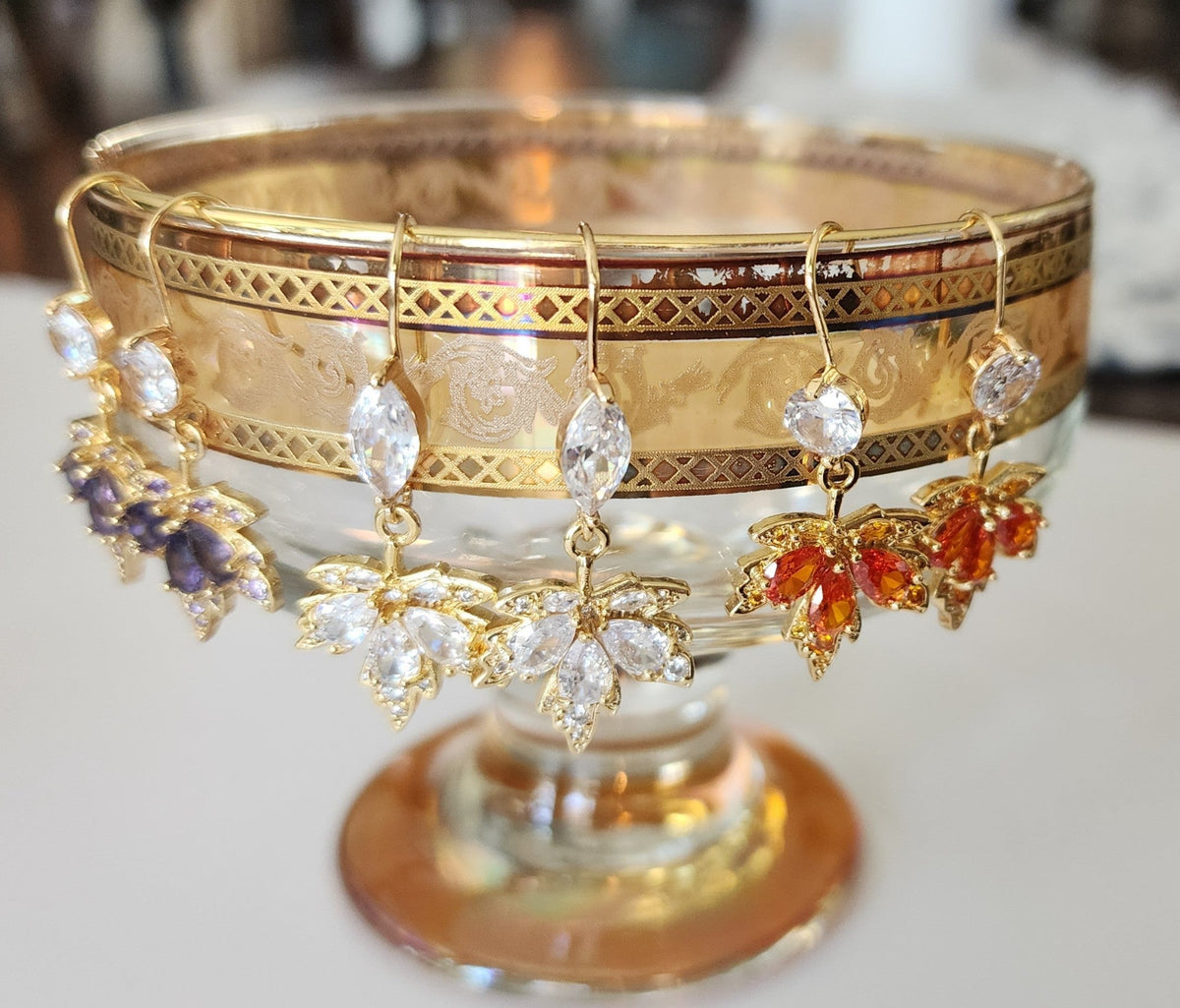 Set of maple leaf earrings with various color crystals on a decorative stand