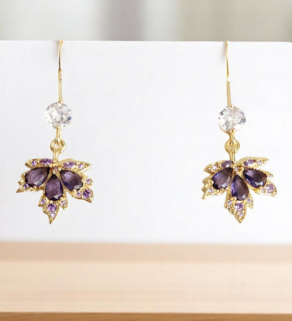 Gold maple leaf earrings with purple and clear gemstones on a white background