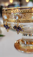 Gold maple leaf earrings with purple crystals on a decorative stand