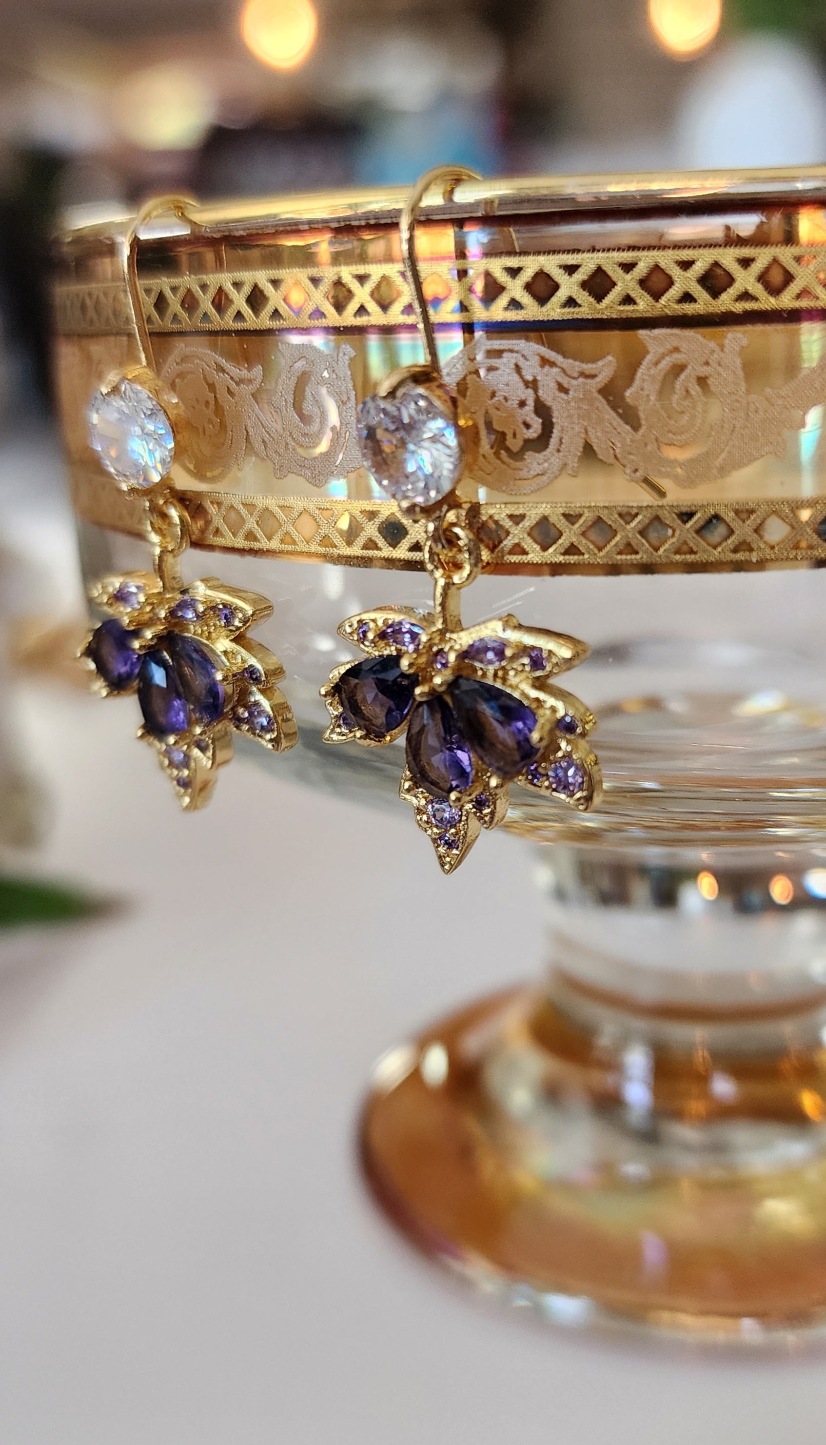 Gold maple leaf earrings with purple crystals on a decorative stand