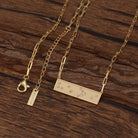 Gold necklace with a rectangular Braille He>i pendant on a wooden surface