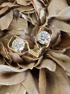 A pair of 14k gold pickleball paddle earrings with round clear diamond gemstones, displayed on a textured beige fabric flower background.