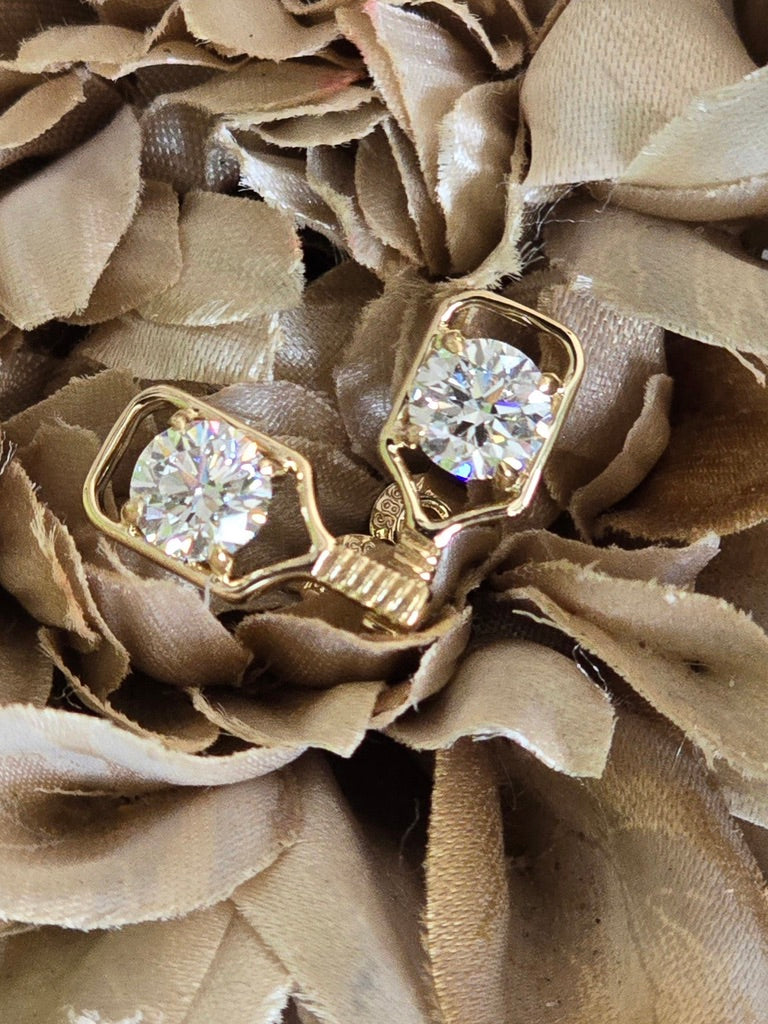 A pair of 14k gold pickleball paddle earrings with round clear diamond gemstones, displayed on a textured beige fabric flower background.