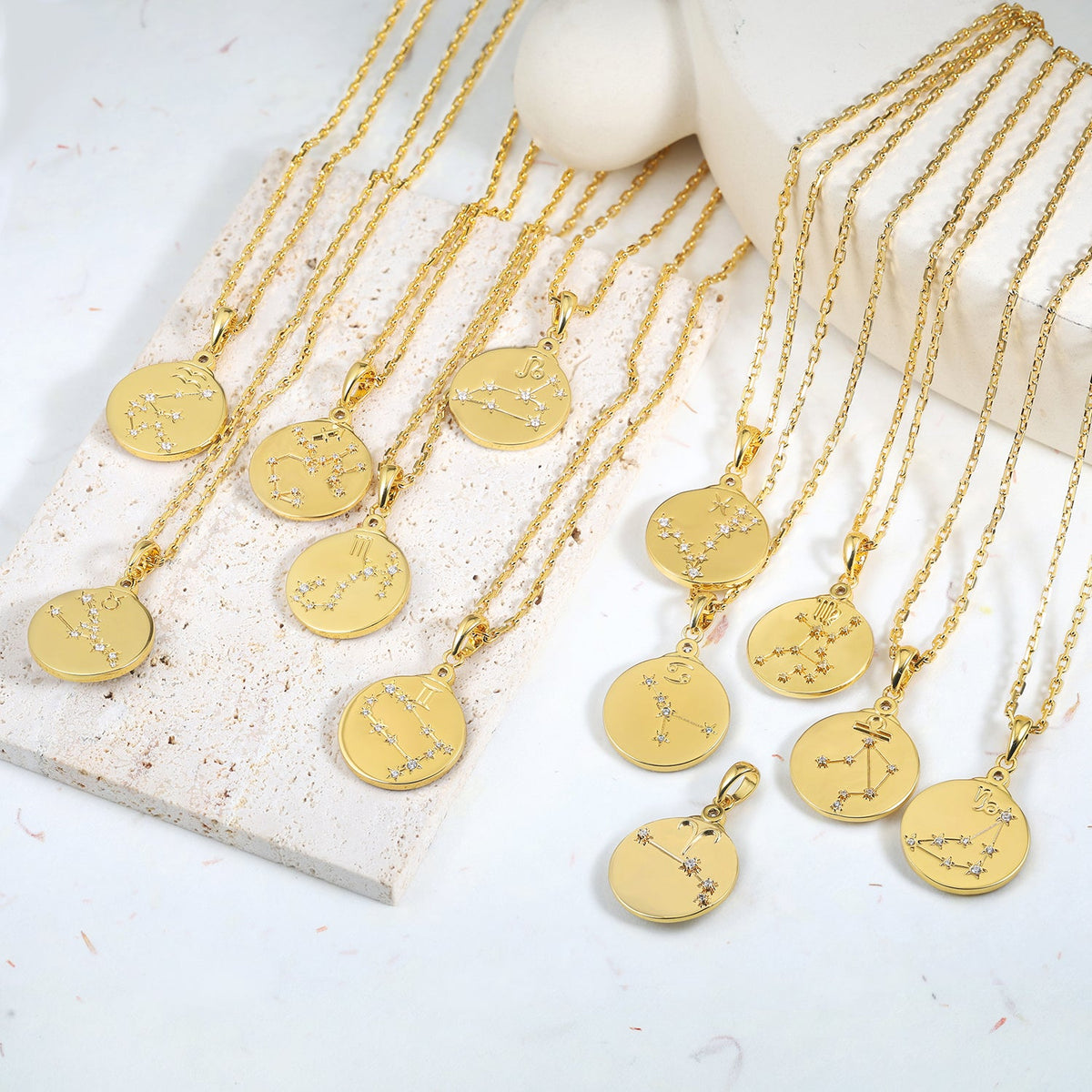 Gold necklaces with zodiac constellation pendants on a white surface