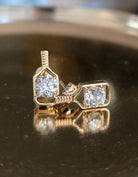 A pair of solid gold pickleball paddle post earrings with round-cut clear diamond gemstones in a bezel setting, displayed on a reflective dark surface.