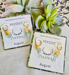 Peridot birthstone August earrings on cards with 'Everwild' branding and 'August' text, surrounded by greenery.
