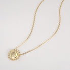 Gold necklace with a circular sunburst pendant etched with friendship symbol on a white background