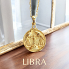 Gold Libra zodiac pendant showing two ravens on a scale necklace on a wooden surface