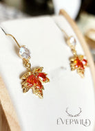 Maple leaf earrings with orange gemstones on a white surface