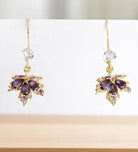 Gold maple leaf earrings with purple and clear gemstones on a white background