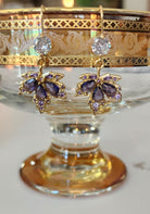 Pair of gold and purple maple leaf earrings on a decorative stand