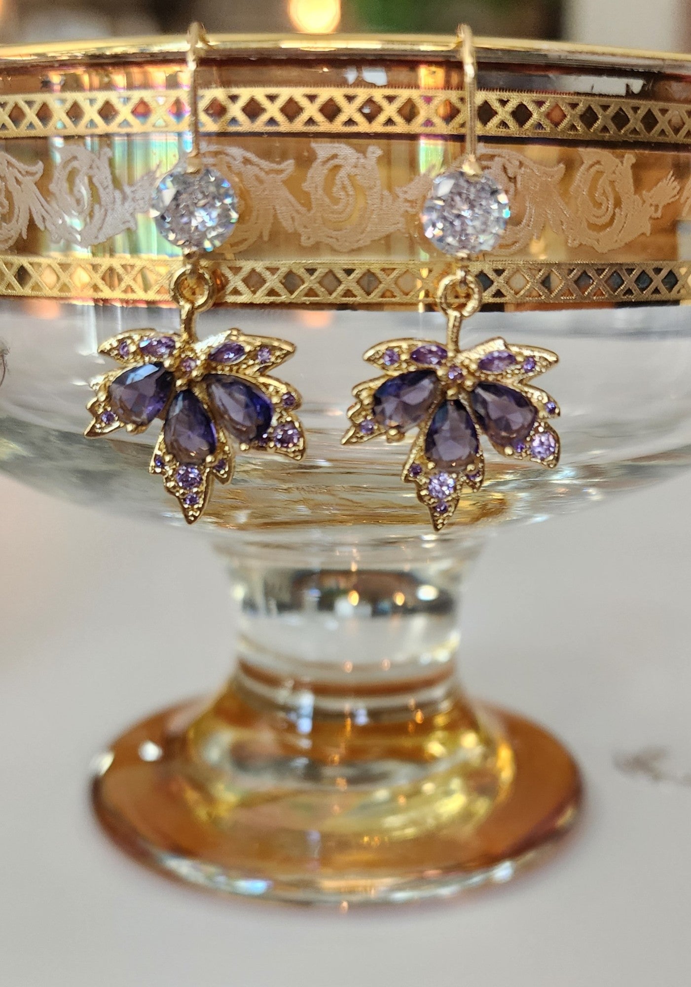 Pair of gold and purple maple leaf earrings on a decorative stand